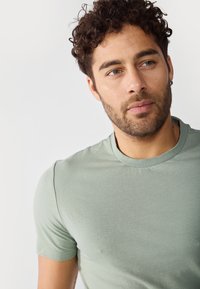 Lys grønn bomulls t-skjorte med klassisk rund hals og korte ermer. Jevn tekstur, tettsittende design.