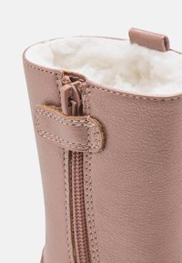 Roze faux leren laars met een fluffy interieur, zijritsopening en contrasterende stiksels langs de naden.