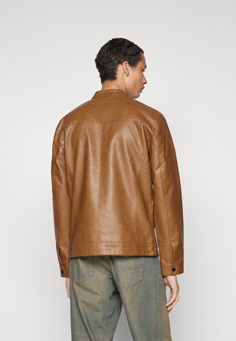 Chaqueta de cuero marrón con un corte relajado, con cuello tipo punta y puños con botones, combinada con pantalones vaqueros de mezclilla de color azul claro.