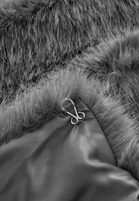 Gray faux fur fabric with a soft texture, featuring a metal hook and a smooth, dark backing. Distinctive long fibers along the edge.