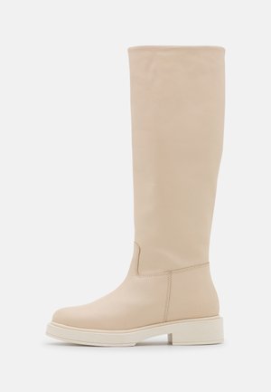 Hoher beiger Lederstiefel mit niedrigem Blockabsatz und abgerundetem Zehenbereich, glatter Textur und minimalen Nähten vor weißem Hintergrund.
