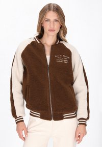 Brun og creme faux shearling bomberjakke med lynlås foran, to sidelommer, stribede manchetter og broderet detalj på brystet.