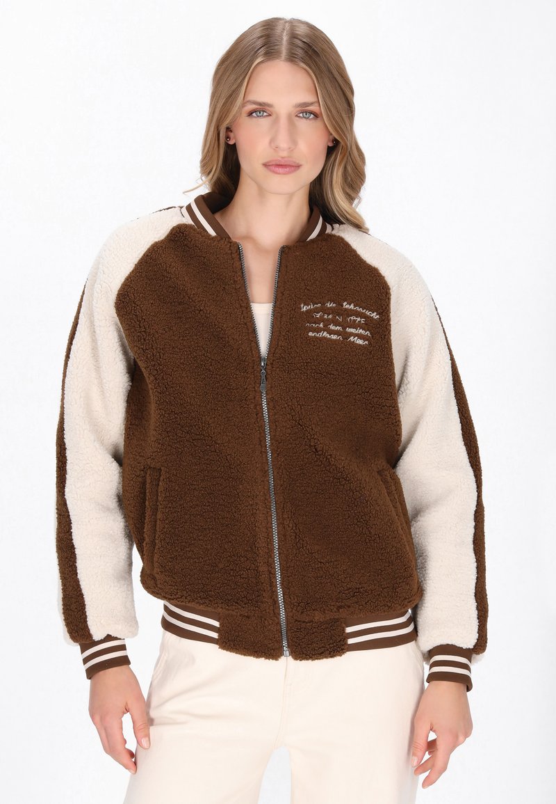 Brun og creme faux shearling bomberjakke med lynlås foran, to sidelommer, stribede manchetter og broderet detalj på brystet.