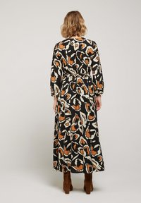 Robe longue noire avec un motif abstrait orange et blanc, taille froncée et longues manches bouffantes, portée avec des bottes marron.