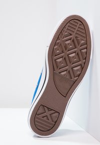 Blå canvas-sneakers med en vit gummisula. Har en strukturerad brun yttersula med diamantformade mönster, märkt med "Converse All Star."