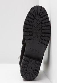 Semelle de basket en daim noir avec motifs antidérapants en caoutchouc texturé et logo DKNY en relief ; bord enveloppé pour une durabilité accrue.