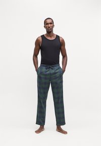 Zwarte tanktop en groene geruite pyjamabroek met blauwe en paarse accenten. De broek heeft een elastische tailleband en steekzakken.