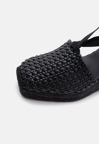 Sandale espadrille noire tissée à bout fermé avec avant carré, semelle tressée et bride à nouer à la cheville sur fond blanc.