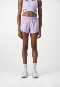 Pantalones cortos deportivos de un ligero color púrpura con cinturilla elástica, combinados con una camiseta deportiva a juego que presenta detalles recortados. Zapatillas blancas completan el atuendo.