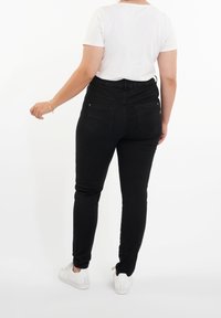 Černé skinny džíny s vysokým pasem a dvěma zadními kapsami, doplněné bílým tričkem s krátkým rukávem a bílými teniskami.