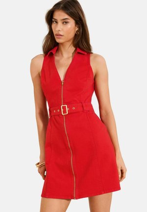 Donna che indossa un vestito rosso senza maniche con cerniera frontale e cintura abbinata, accessoriata con orecchini a cerchio dorati e bracciale.