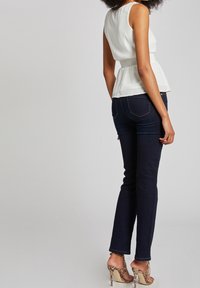 Bílý bezramenný peplum top s texturovaným detailem v oblasti pasu, doplněný tmavě modrými úzkými džíny a vzorovanými sandály na podpatku.