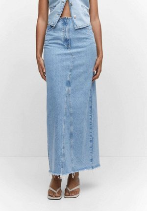 Femme portant une jupe longue en jean bleu clair avec un ourlet brut et un gilet en jean assorti, debout devant un fond blanc uni.