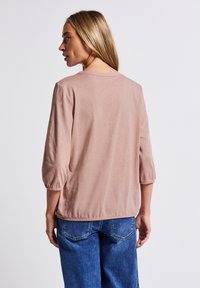Chemise rose clair à manches courtes avec une coupe décontractée et des manches froncées, fabriquée dans un matériau doux. Accordée avec un jean en denim bleu.