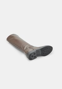 Bota de cuero marrón hasta la rodilla con textura lisa, suela de goma plana con dibujos circulares y cremallera lateral para cierre.