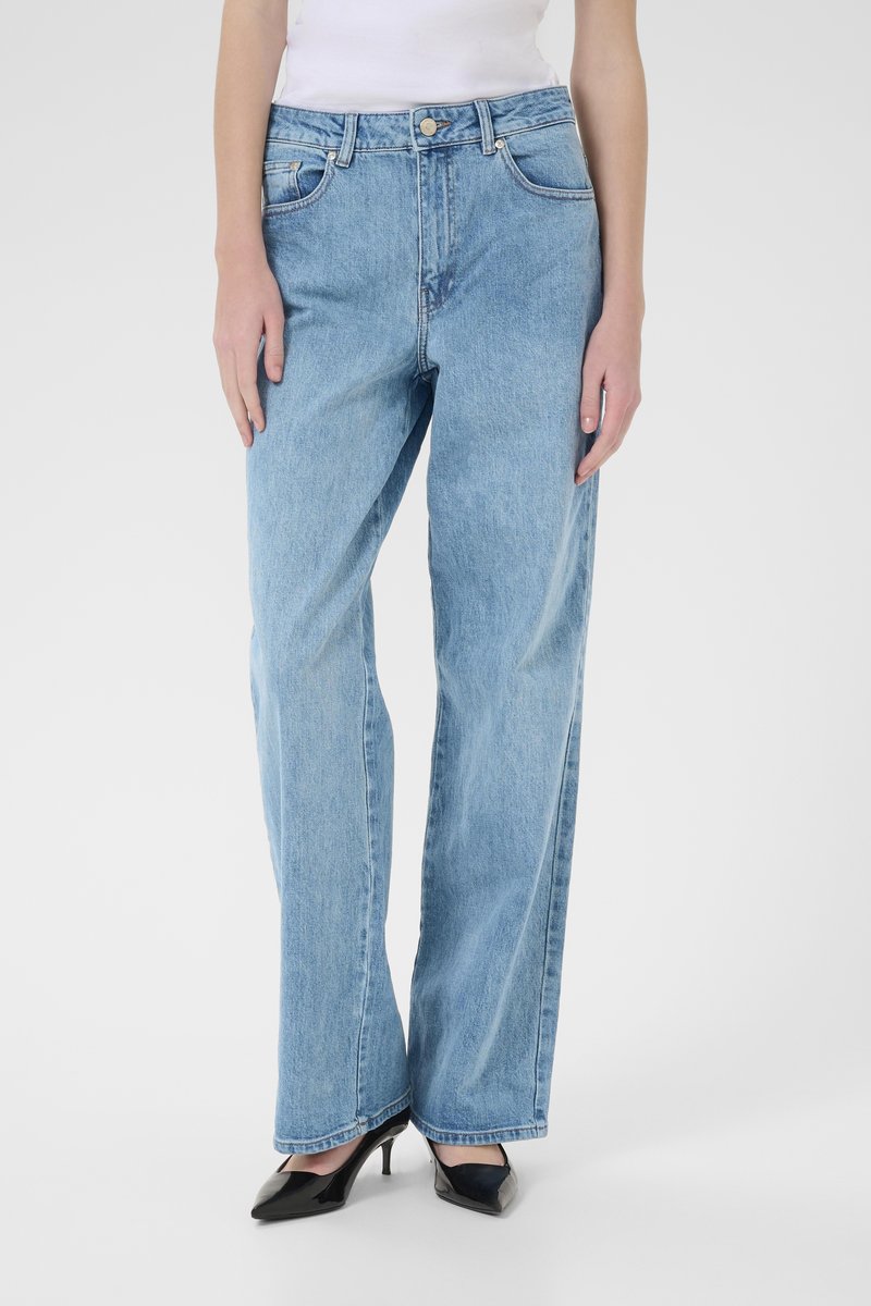 Lyseblå brede jeans laget av denim, med høy midje, frontlommer og synlige sømmer. Brukt med svarte høyhælte sko.