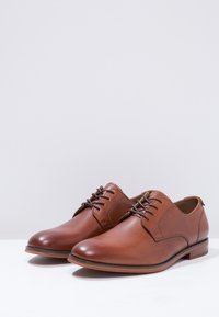 Chaussures habillées en cuir marron avec une finition lisse, un bout rond et un design lacé traditionnel avec des lacets foncés et un petit talon empilé.