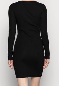 Svart ribbad bodycon-klänning med långa ärmar, som har en rund halsringning och en figurnära silhuett som framhäver kroppen.