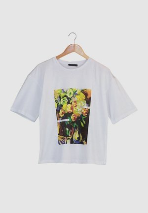 T-shirt en coton blanc à manches courtes avec un motif floral coloré imprimé sur le devant, représentant des roses et des fleurs jaunes.