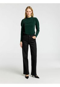 Grön, långärmad topp med subtil glitter och puffärmar, i kombination med svarta, rakbeniga jeans och svarta, spetsiga klackar.