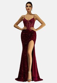 Frau in einem bodenlangen, tiefroten Paillettenabendkleid mit einem Oberschenkelspalte, Spitzenbustier, dünnen Trägern und silbernen High Heels.
