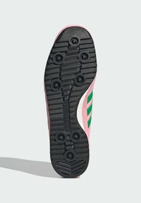 Sola de sapatilha atlética em rosa com padrão de tração em borracha preta. Apresenta pinos circulares para aderência e um detalhe em onda branca de lado.