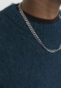 Dunkelblauer Strickpullover mit strukturierter Oberfläche, mit rundem Halsausschnitt und einer silbernen Kette, die über einem schwarzen T-Shirt liegt.