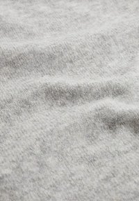 Tissu gris clair avec une surface douce et texturée présentant un motif tissé subtil ainsi que de légères ondulations. Le matériau semble être en maille ou en polaire.