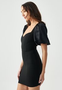 Zwarte bodycon jurk met een textuurstof, diepe V-halslijn, aansluitende pasvorm en pofmouwen in een glanzend materiaal.