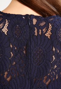 Granatowa sukienka koronkowa z kwiatowymi wzorami, teksturowanym wykończeniem i dyskretnym zapięciem na zamek z tyłu.