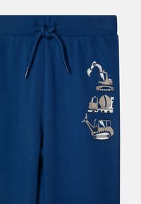 Marineblaue Sweatpants mit einem strukturierten Bund und Zugband. Sie haben drei bedruckte Designs von Baustellenfahrzeugen in Creme und Grau.