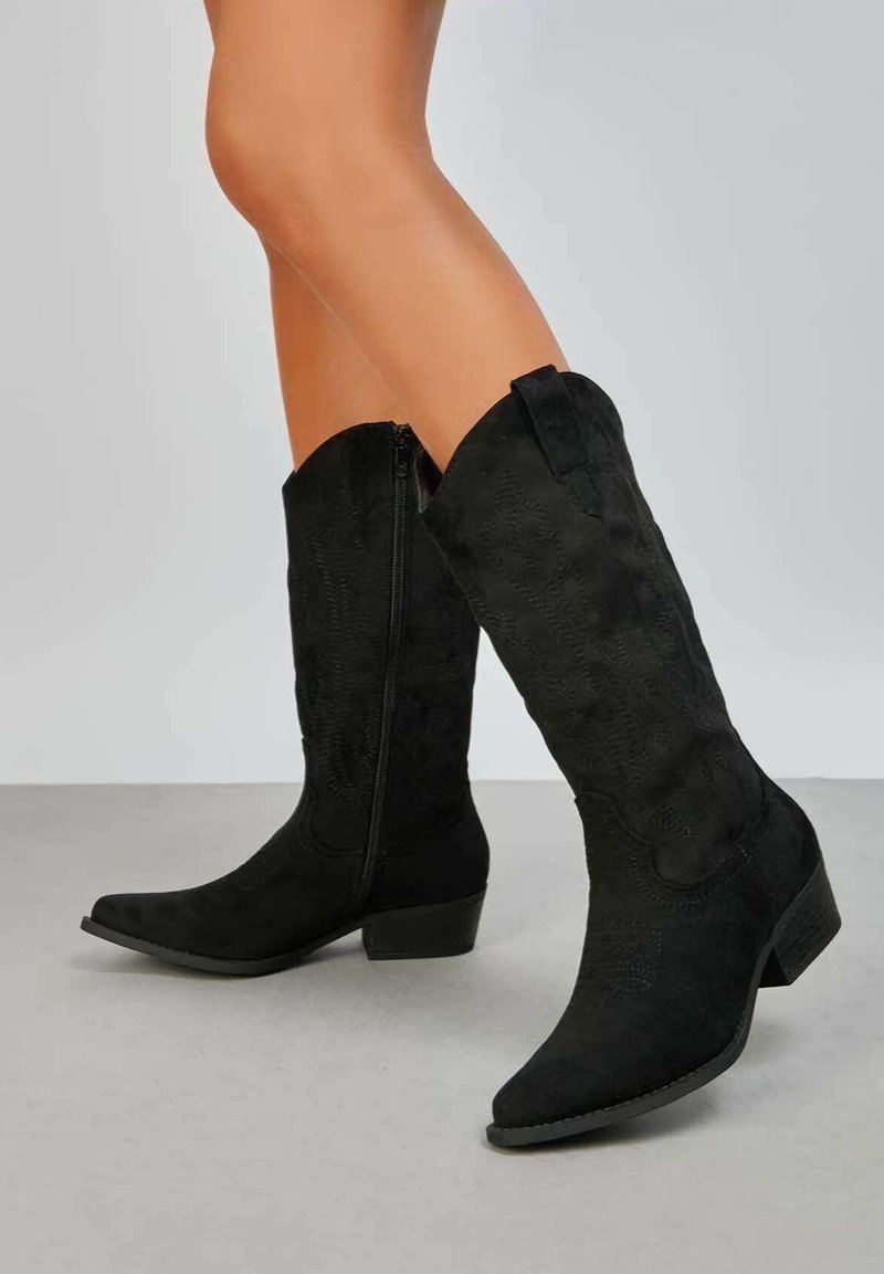 Bottes de cowboy en daim noir avec un bout pointu, hauteur mi-mollet, motifs texturés et une fermeture éclair latérale. Talon bas et carré.