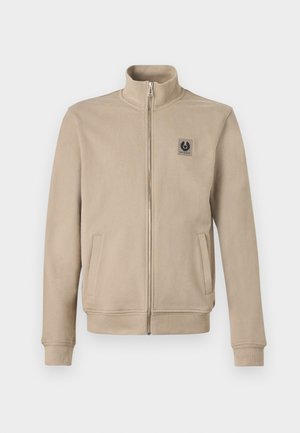 Beige lynlåsjakke med høj krave, to sidelommer, ribbede manchetter og kant samt et lille logo på venstre bryst.