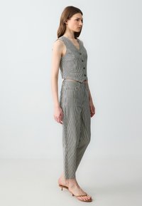 Gilet corta a righe grigie e bianche con scollo a V, abbinato a pantaloni a vita alta coordinati. Presenta bottoni e una vestibilità sartoriale.