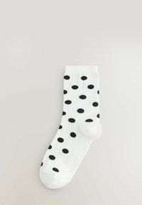 Biała skarpetka w czarne kropki. Posiada ściągacz i gładką teksturę. Standardowy kształt z wzmocnionym palcem dla zwiększonej trwałości.