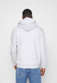 Sweat à capuche gris avec une grande capuche ajustable, doté d'une texture douce et de poignets côtelés. Porté avec un jean en denim bleu clair.