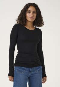 Maglietta nera a maniche lunghe, aderente e realizzata in materiale morbido, con scollo rotondo e maniche senza cuciture, abbinata a jeans di jeans blu.