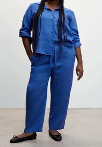 Chemise en lin bleue avec boutons sur le devant, manches longues et coupe décontractée, associée à un pantalon large assorti. Des ballerines noires complètent la tenue.