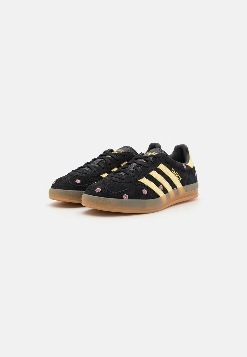 Sneaker in suede nero con dettagli a tre strisce gialle, ricami floreali sulla parte superiore e suola in gomma naturale. Design a profilo basso.