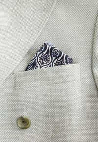Blazer gris clair à carreaux avec un mouchoir de poche noir, blanc et or à motif, glissé dans la poche poitrine.