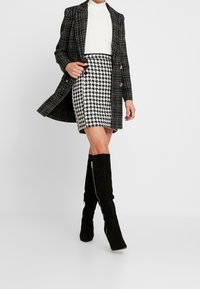 Black and white houndstooth skirt paired with a black plaid coat. Knee-high black suede boots with a side zipper detail. White top.