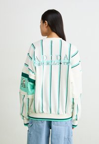 Λευκή φούτερ μπλούζα με πράσινες κάθετες ρίγες, με ανάγλυφο το "ADIDAS ORIGINALS", γραφικό στην μανσέτα και ριμπ μανσέτες και στρίφωμα.