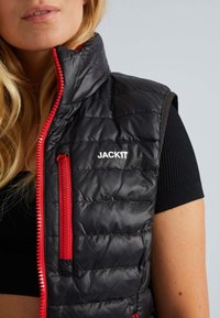 Schwarze, gesteppte Weste mit hohem Kragen und roten Zipper-Akzenten; verfügt über ein Logo auf der linken Brust und eine seitliche Reißverschlusstasche.