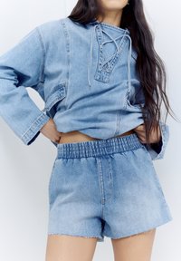 Denimoutfit som består av en ljusblå, avslappnad pullover med snörning i halsen och matchande högmidjade shorts med elastisk midja.