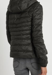 Czarna kurtka puchowa z kapturem, pikowany wzór, elastyczne mankiety i dopasowany krój. Gładka, błyszcząca tekstura powierzchni.