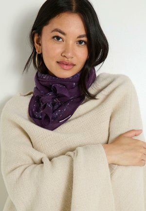 Bufanda púrpura con un diseño de paisley, llevada de manera suelta alrededor del cuello, combinada con un suéter de punto color crema. Textura suave, estilo casual.