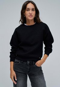 Černé strukturované mikina s kulatým výstřihem, spadlými rameny a žebrovanými manžetami. Přiřazeno k tmavě šedým džínům. Poznámka: jemný detail loga.