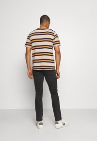 Camiseta a rayas en beige, marrón y naranja, con cuello redondo y mangas cortas. Combinada con jeans negros y zapatillas blancas.