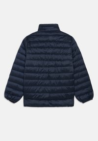 Ναυτικό puffer μπουφάν με επενδυμένο σχέδιο, όρθιο γιακά και ελαστικές μανσέτες. Λείο υφή με οριζόντια ραφή λεπτομέρειας.