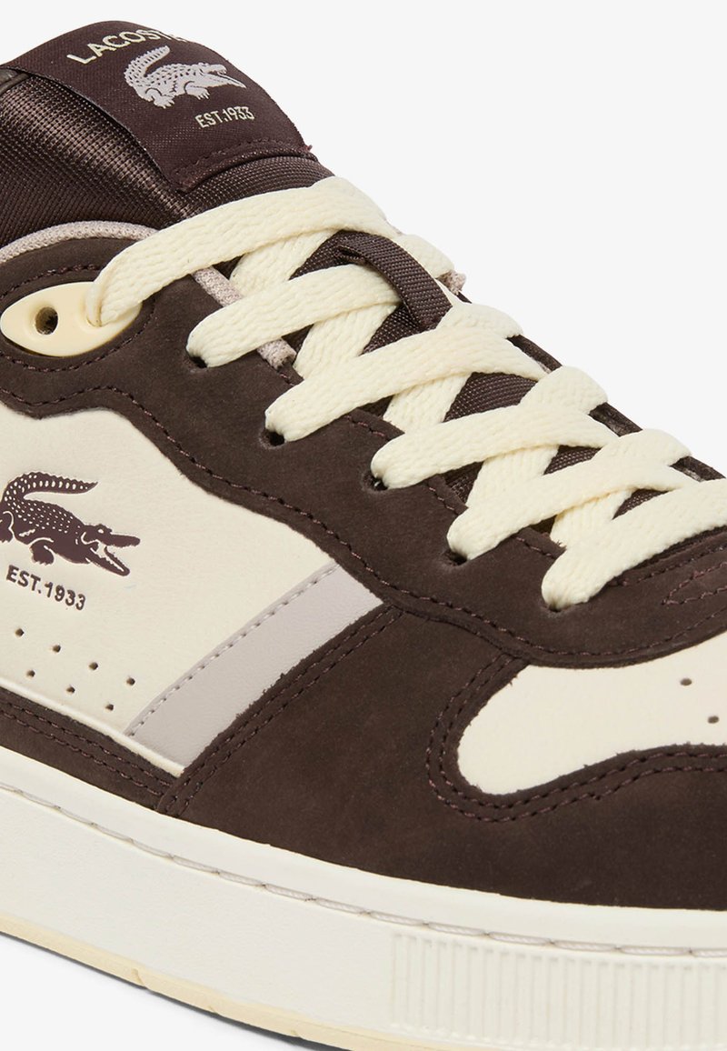 Lacoste-Sneaker in Braun und Cremeweiß mit cremefarbenen Schnürsenkeln, Krokodil-Logo und dem Schriftzug "EST. 1933" an der Seite und auf der Zunge.